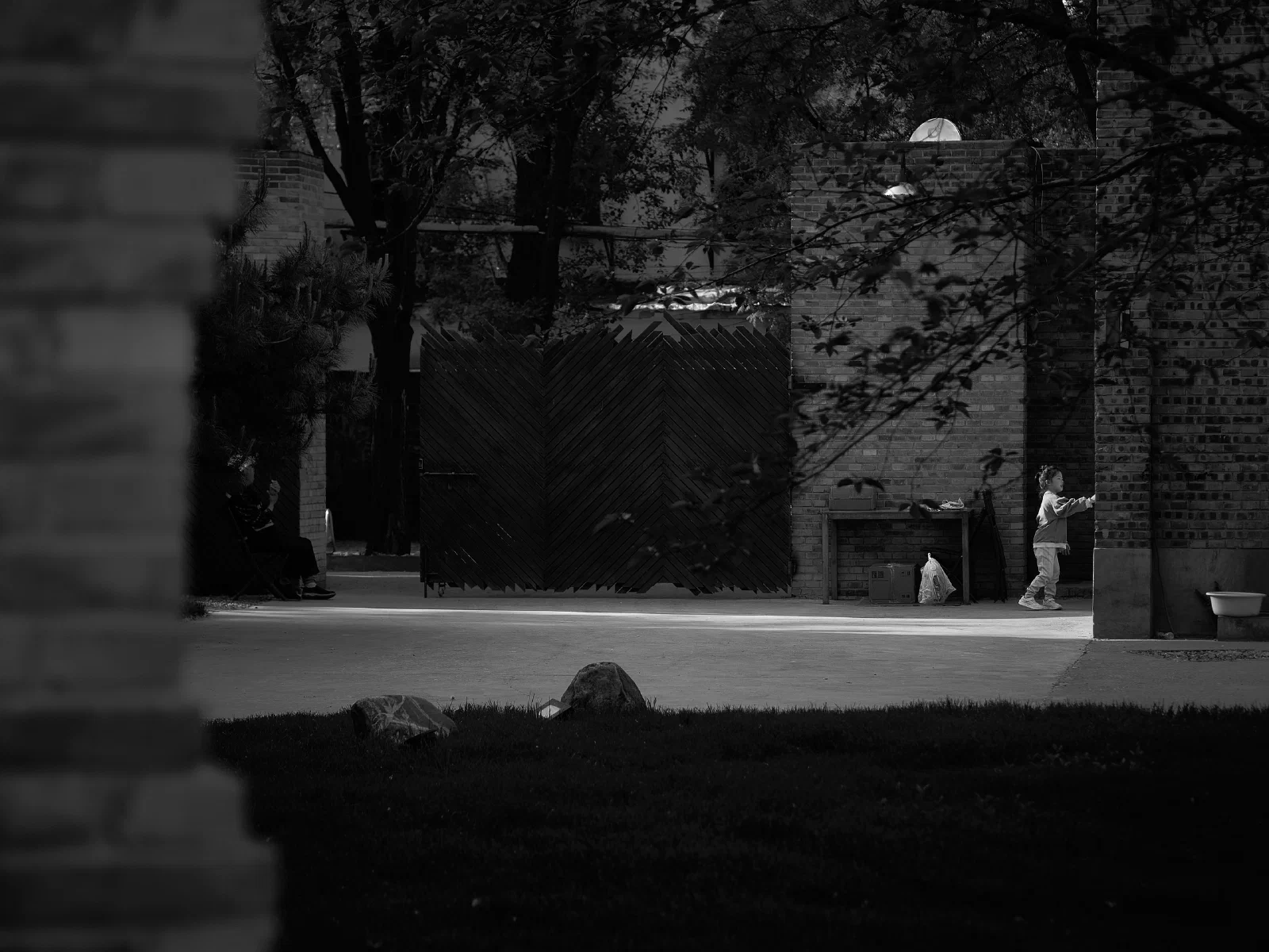 A child in the light and seated figures in the shadows of a courtyard.