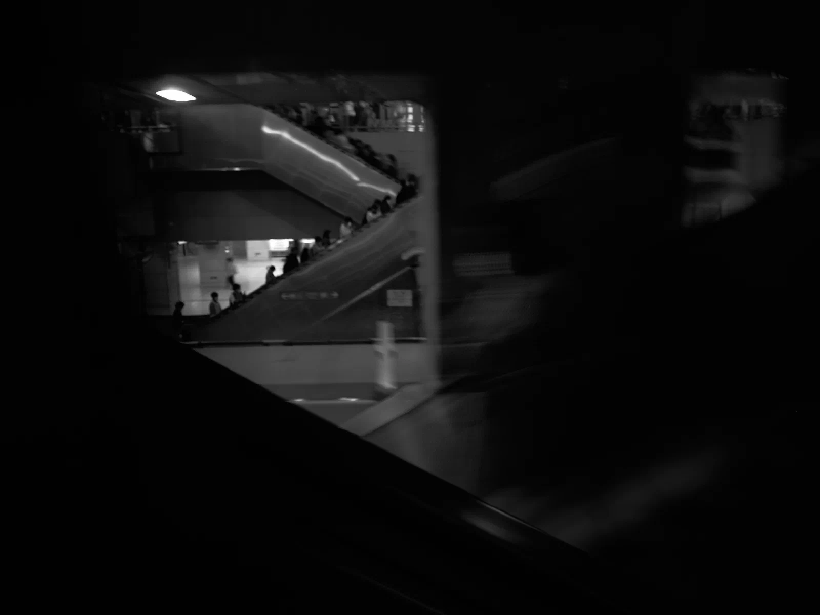 A line of people on an escalator, seen from the dark.