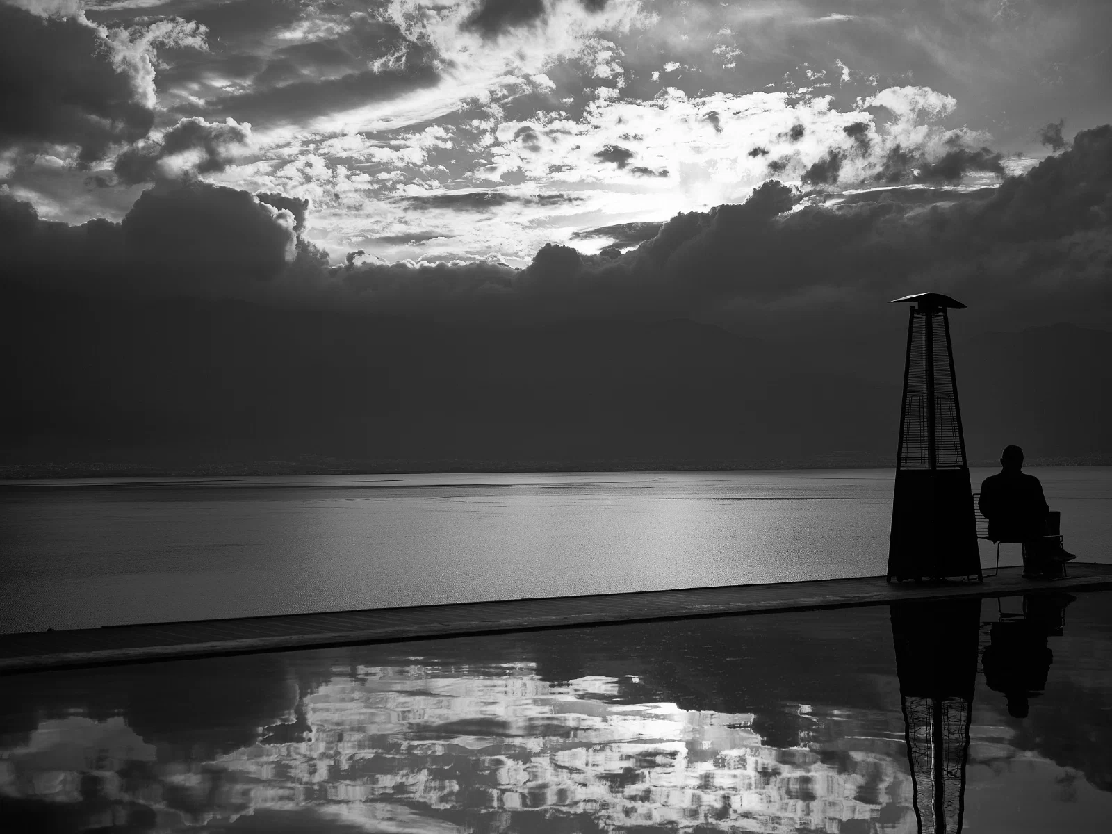 A seated figure beside the water and a reflection below.