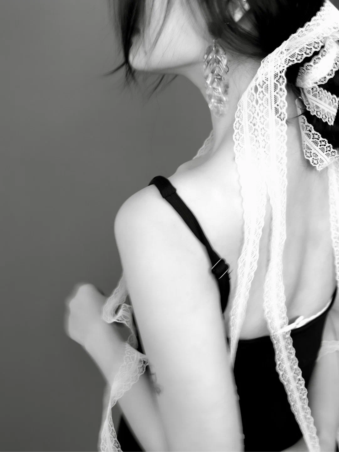 Close view of a shoulder and neck from behind, with white lace ribbons hanging from the hair.