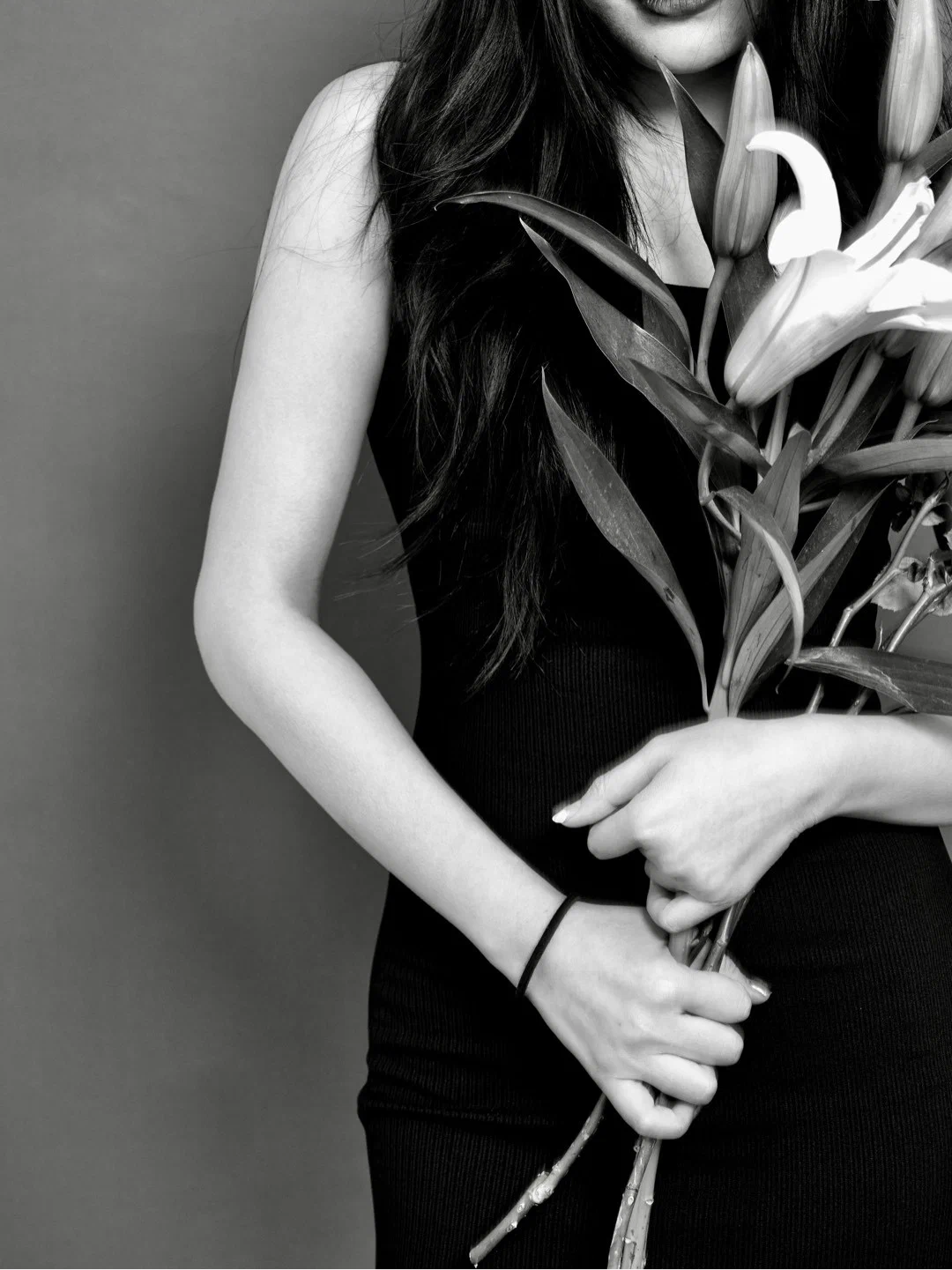 Close view of a torso and hands holding lily stems against a dark dress.